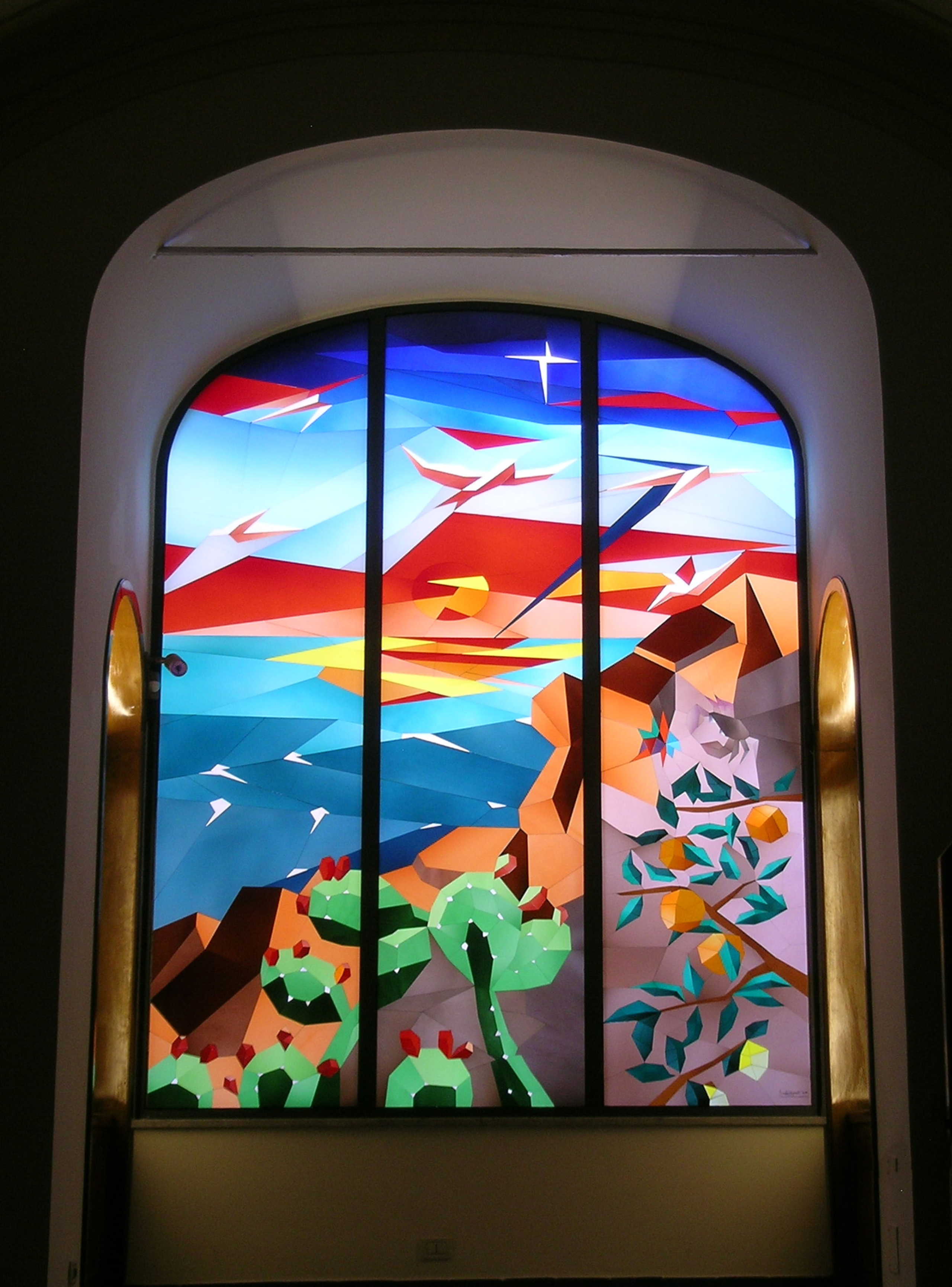 Farbenfrohes Buntglasfenster mit abstraktem Design in einer bogenförmigen Rahmenstruktur, beleuchtet von hinten.