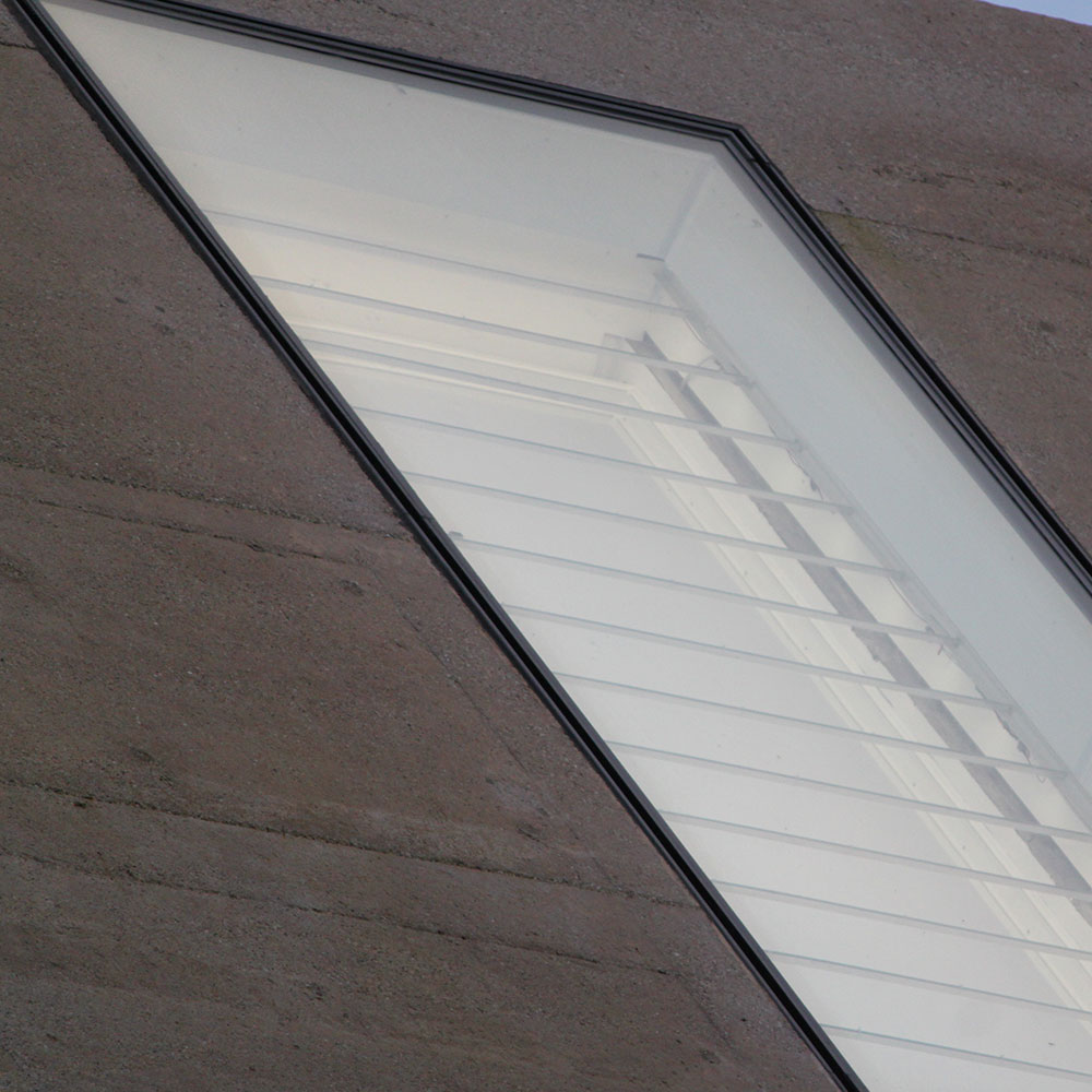 Detailansicht eines modernen Kirchenfensters mit auffälliger, verzerrter Form und Lichtreflexionen, eingebettet in dunkle Steinfassade.
