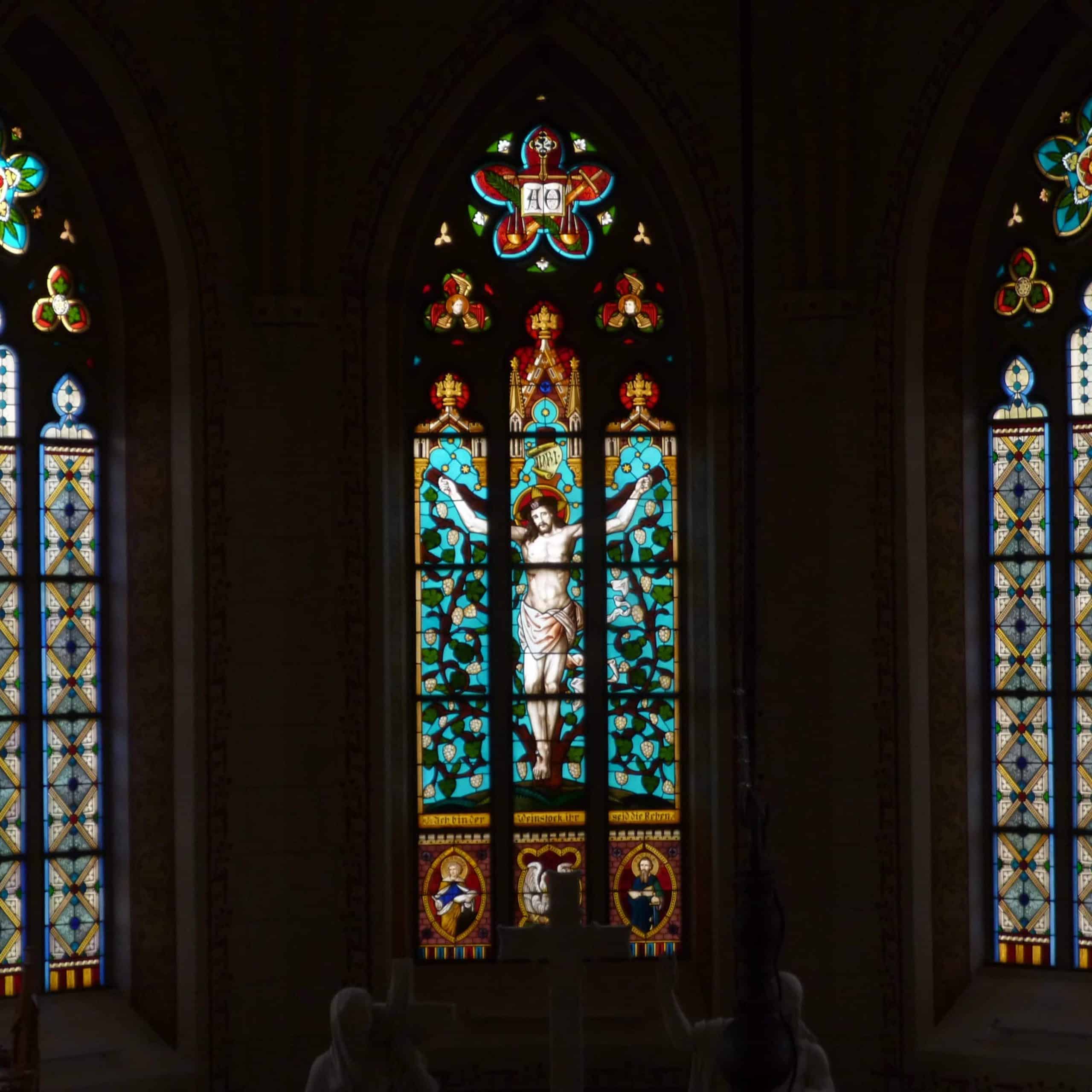 Farbenprächtiges Kirchenfenster mit Darstellung von Jesus und ornamentalen Mustern in einer stilvollen Kirche.