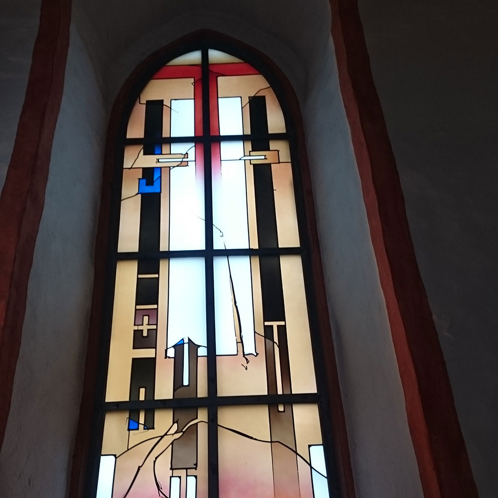 Kirchenfenster mit modernem Glasmalerei-Design, abstrakte Formen in Weiß, Blau und Rot mit Kreuzmotiv in der Mitte.