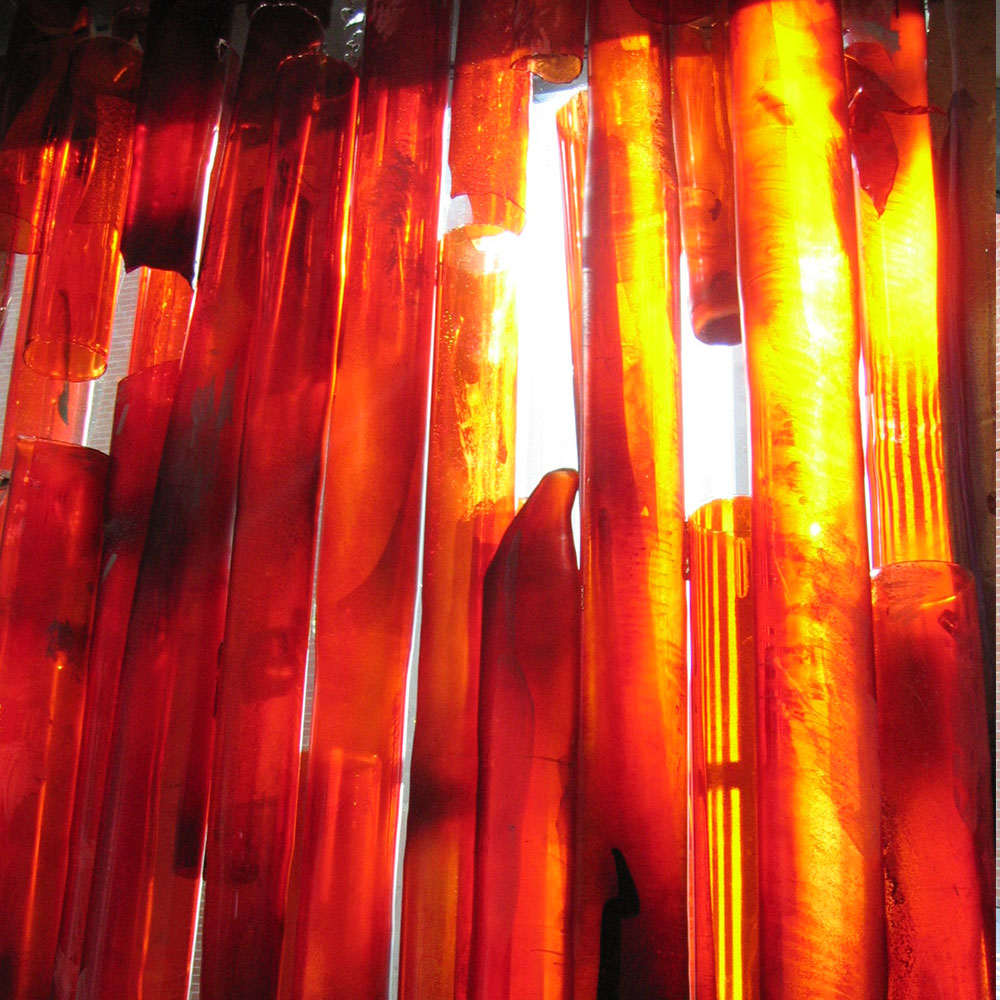 Vertikale, transluzente rote und orange Glasstäbe, beleuchtet, erinnern an Bambuswald, installiert am Flughafen München.