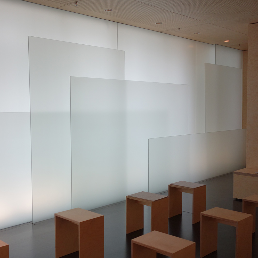 Moderne Kapelle mit minimalistischem Design, bestehend aus matten Glaswänden und einfachen Holzbänken.