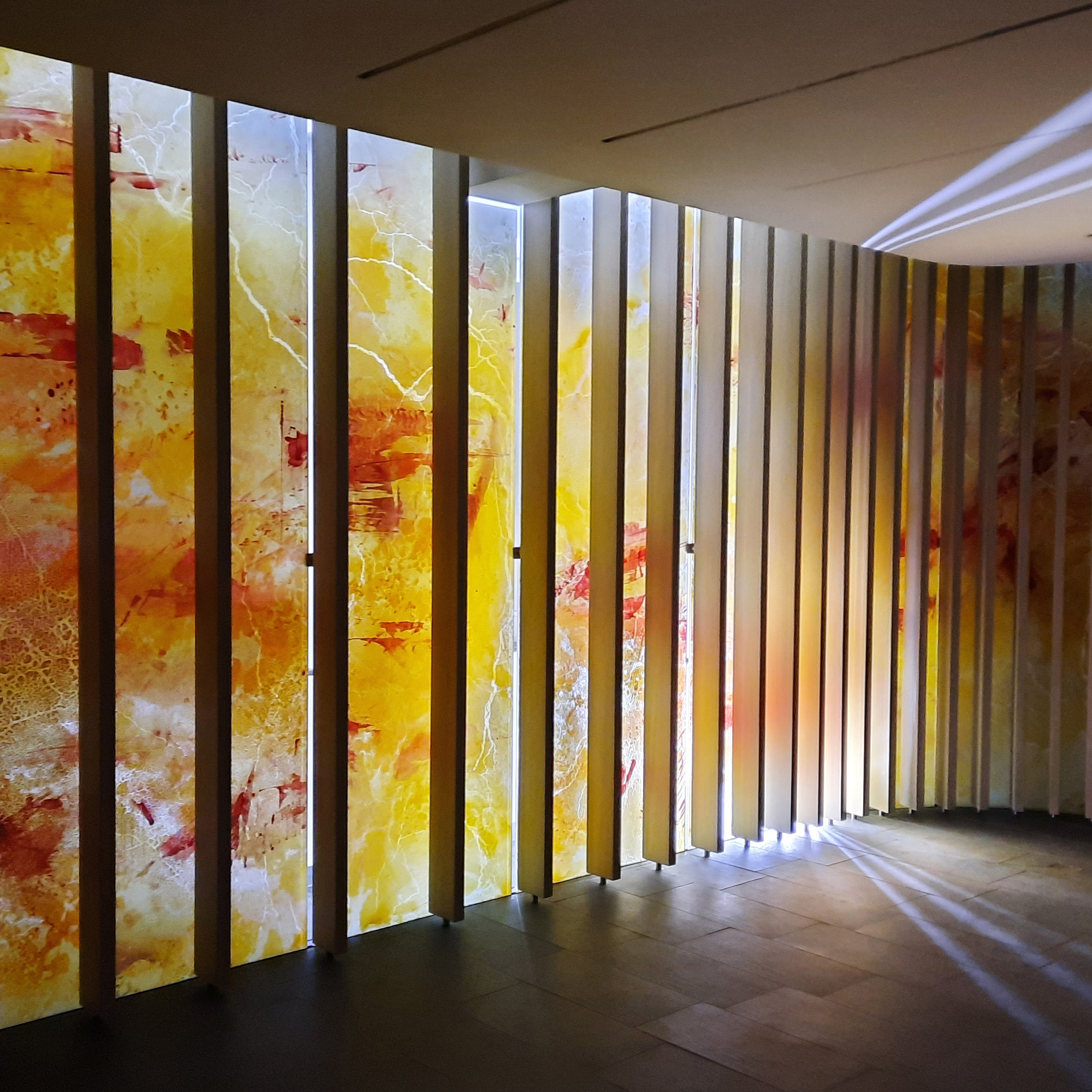 Stehende beleuchtete Glasplatten mit gelb-roten Farbmustern, erzeugen eine warme, atmosphärische Beleuchtung im Raum.