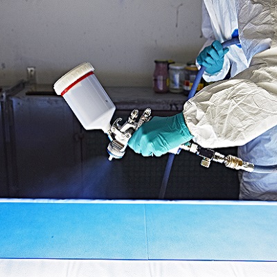 Close up of airbrush pistol Person in Schutzkleidung führt Airbrush-Arbeiten an Glas aus, blauer Farbnebel im Bild sichtbar.