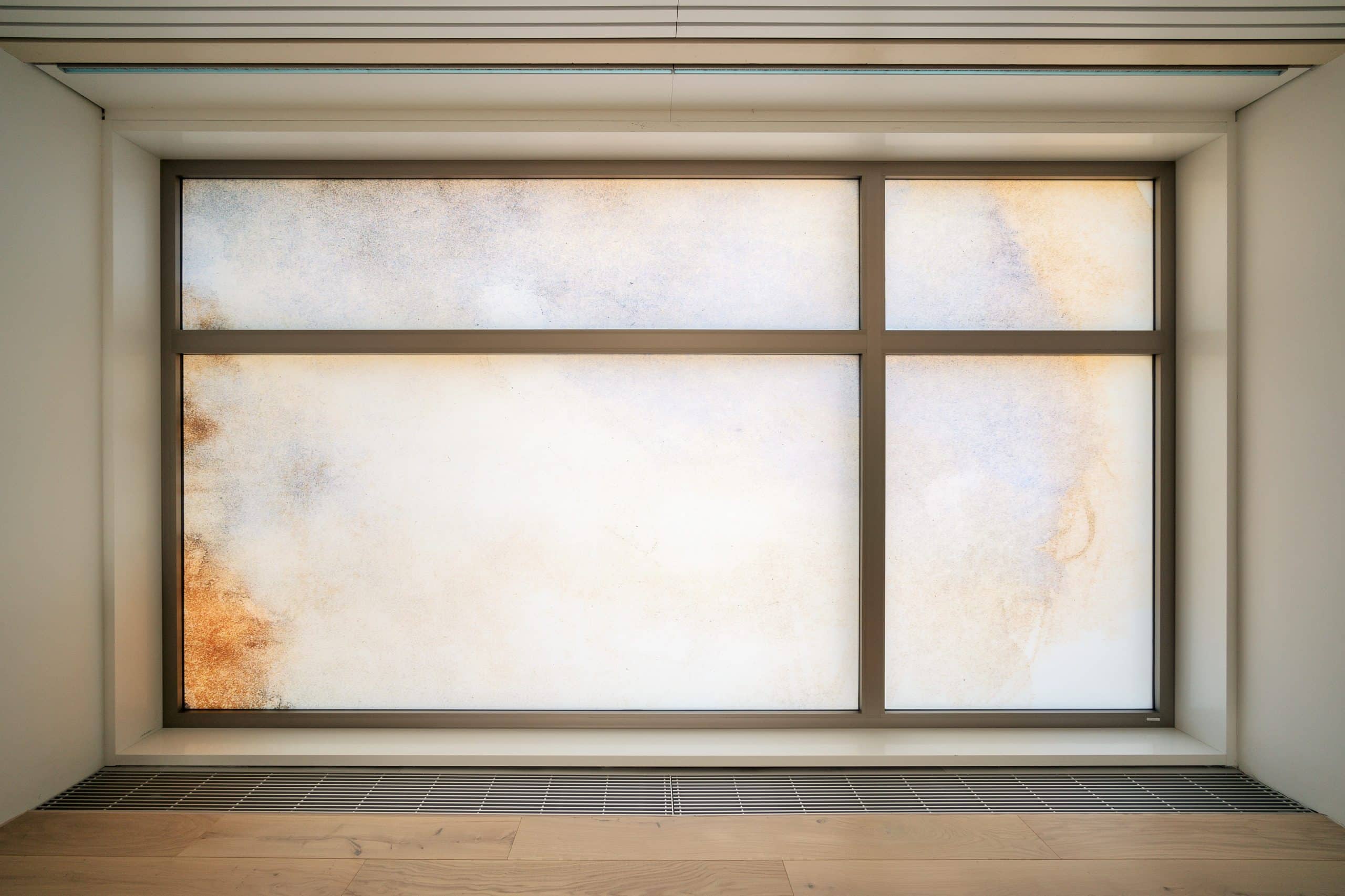 Großes, modernes Fenster mit vier Glaseinsätzen, teils klar, teils mit sanften, abstrakten Farbverläufen in einem hellen Raum.