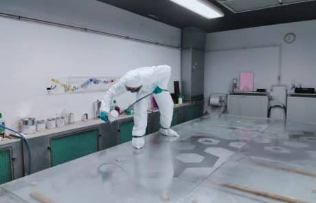 Person in Schutzkleidung verarbeitet Material auf einem großen Arbeitstisch in einem hellen Atelier.