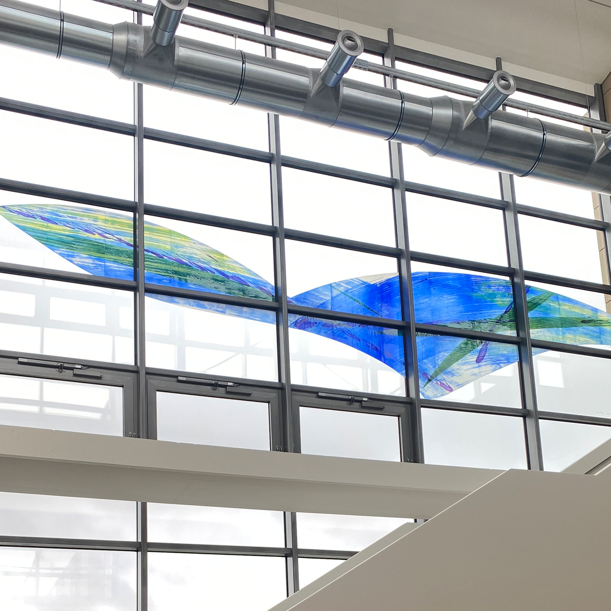 Modern glass art installation in a building, consisting of several colorful glass panels that allow natural light to shine through.