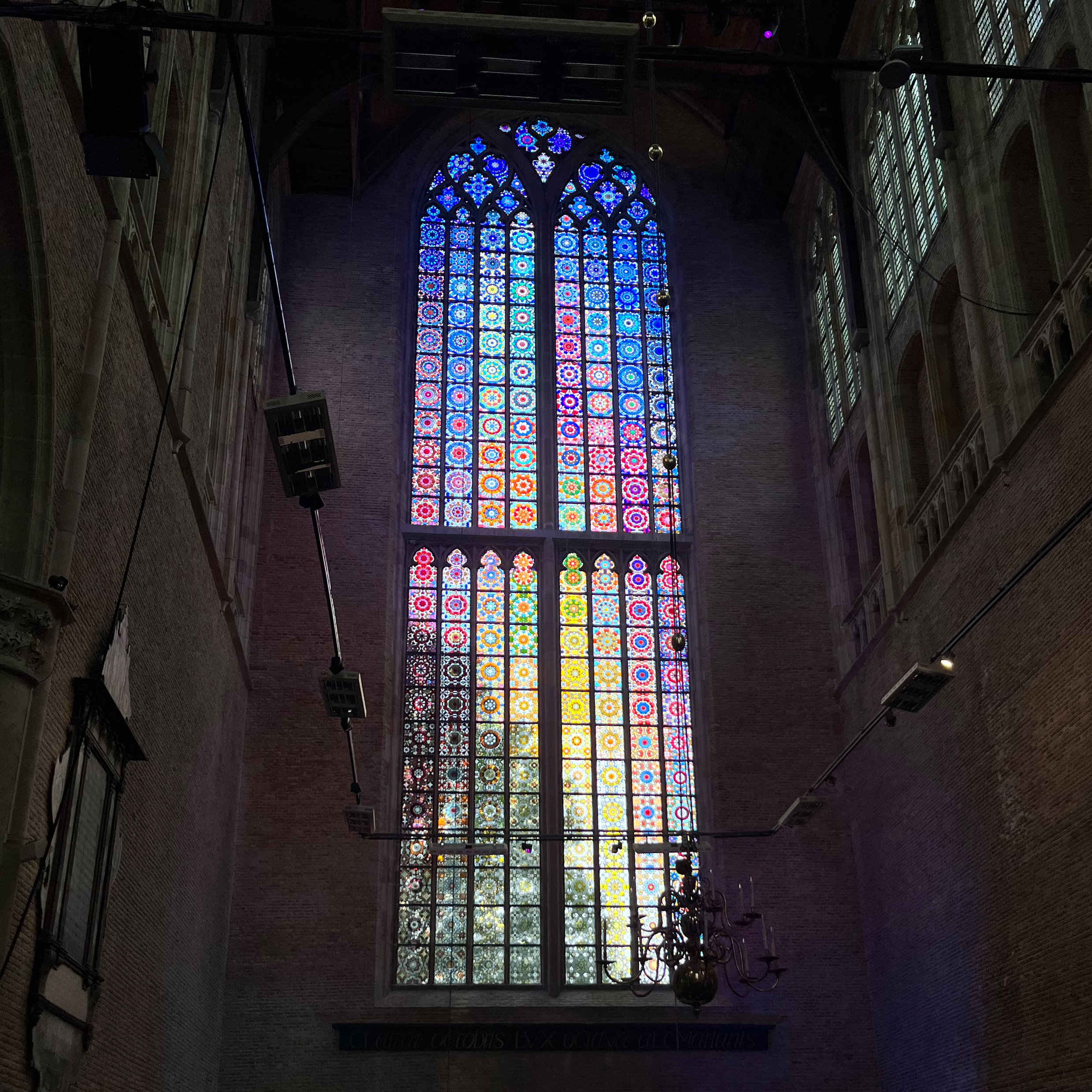 Farbenprächtiges, großes Kirchenfenster mit Ornamenten, durch das Licht in einen dunklen Innenraum fällt.