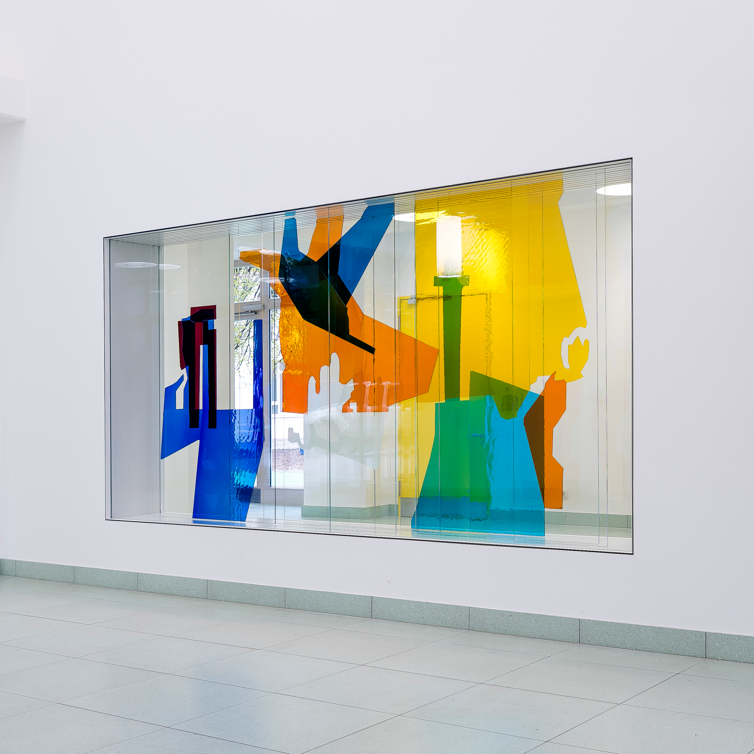Farbenfrohe Glaskunstinstallation in lebendigen Blau-, Gelb- und Orangetönen, ausgestellt in einer hellen Galerie.