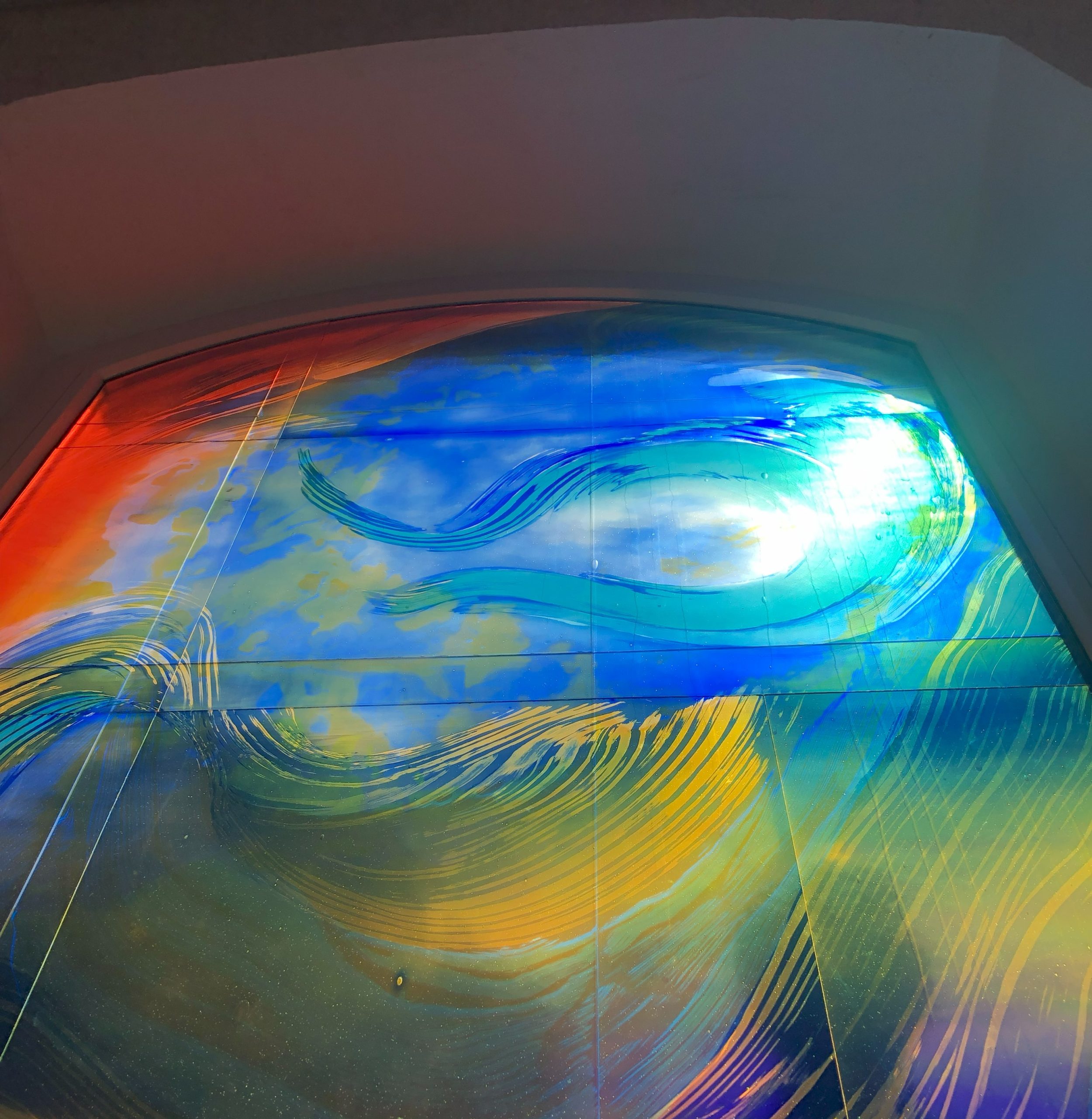 Farbenfrohes Glaskunst-Fenster von Derix mit geschwungenen Linien in Blau, Orange und Gelb. Das Fenster ist in der Kapelle des Pflegeheims Haus Zoffingen.