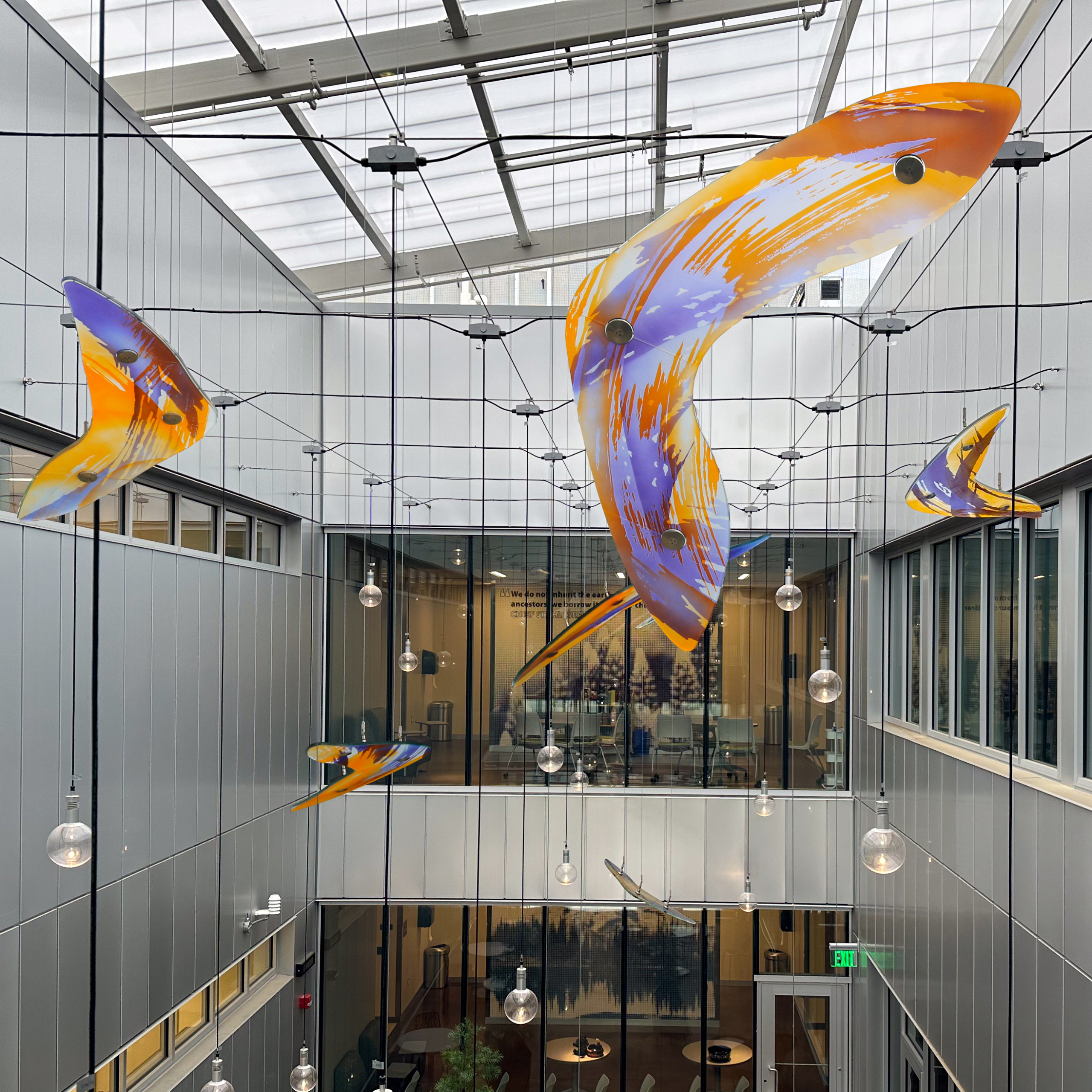 Bunt bemalte Glaskunstwerke in Form von Fischen, aufgehängt in einer lichtdurchfluteten Atrium-Lobby im Lakewood College.