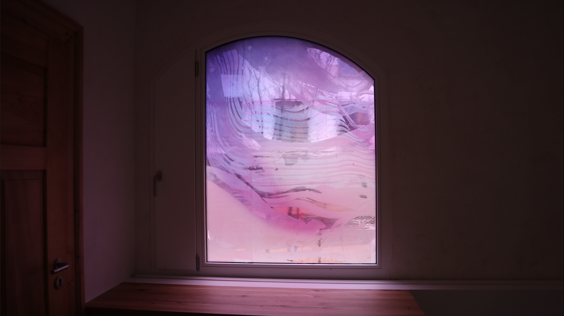 Buntes Glasfenster mit abstrakten Mustern in einem Raum, zeigt das Kunsthandwerk von Derix Glasstudios. Lila Farbtöne bestimmen das Bild.