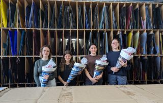 Vier Personen stehen vor einem Regal mit bunten Glasplatten, halten Materialkataloge.