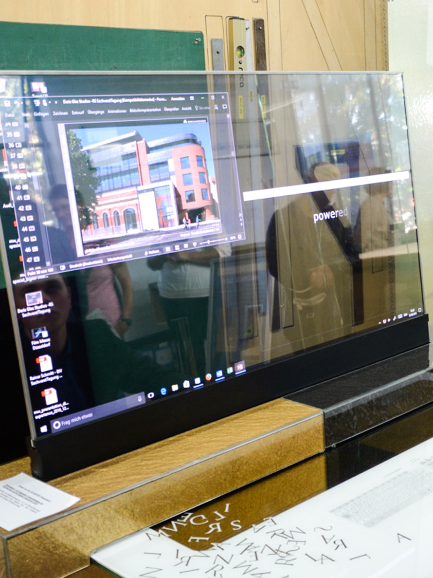 Transparenter Bildschirm auf Schreibtisch zeigt Grafikprogramm, Reflexion einer Person und Interieur im Hintergrund.