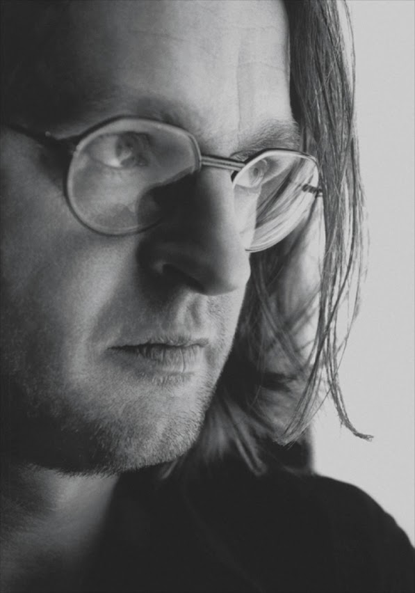 Portrait – Derix Glasstudios Nahaufnahme eines Mannes mit Brille, der ernst seitlich in die Kamera blickt, mit betonten Gesichtszügen und reflektierenden Brillengläsern.