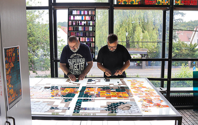 Zwei Männer die an einem Leuchttisch Glasmalereien kontrollieren